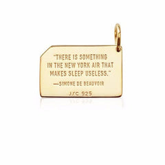Back of gold rectangular charm imprinted with quote: 'There is something in the New York air that makes sleep useless. -Simone de Beavoir'